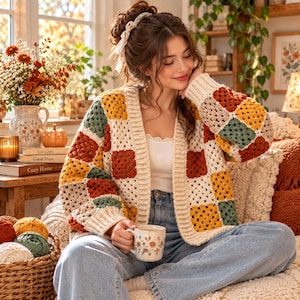 May include: A long-sleeve crochet cardigan featuring a patchwork pattern of square motifs in cream, mustard yellow, burnt orange, and sage green. The garment has a ribbed cream-coloured trim along the front opening, cuffs, and hem, with a buttonless design.
