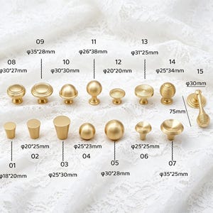 May include: A collection of fifteen gold-toned metal cabinet knobs and pulls in various shapes and sizes, including spherical, cylindrical, and ridged designs. Each piece is labeled with a number and its specific metric dimensions in millimeters.