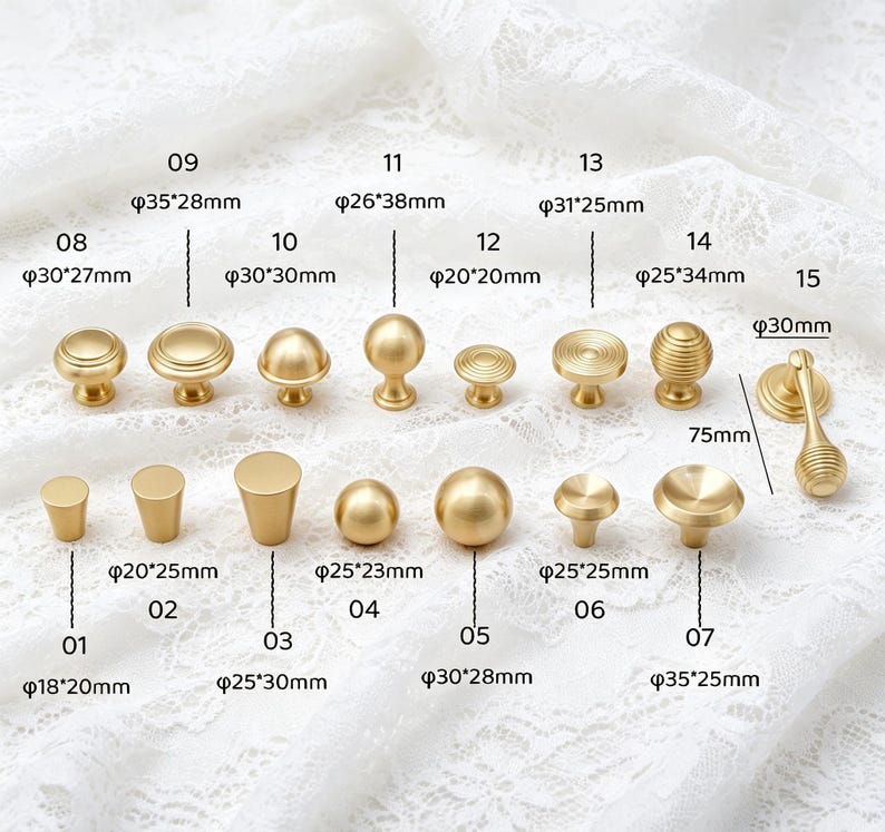 May include: A collection of fifteen gold-toned metal cabinet knobs and pulls in various shapes and sizes, including spherical, cylindrical, and ridged designs. Each piece is labeled with a number and its specific metric dimensions in millimeters.