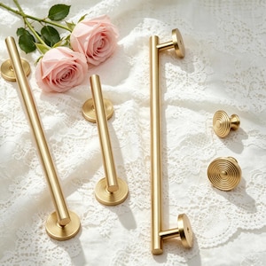 May include: A set of brushed gold cabinet hardware including two long cylindrical bar pulls with circular bases featuring concentric ring detailing and two matching round knobs with the same circular grooved pattern on the face.