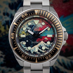 May include: Stainless steel wristwatch with a black and gold bezel. The watch face features a colorful wave design with the word "AUTOMATIC" printed at the bottom. The watch has a silver band.