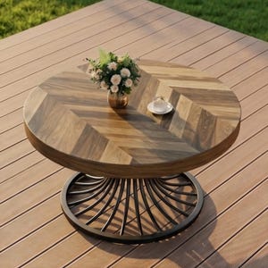 Puede incluir: Mesa de centro redonda de madera con un patrón de espiga en la superficie. La mesa tiene una base de metal oscuro con un diseño curvo. Un pequeño jarrón con flores y una taza de café están sobre la mesa. La mesa está sobre una terraza de madera. Diámetro: aprox. 90 cm.