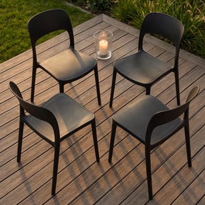 Puede incluir: Cuatro sillas de exterior de plástico negro dispuestas sobre una terraza de madera. Cada silla tiene un respaldo curvo y un asiento cuadrado. Un portavelas de cristal con una vela encendida se encuentra entre dos sillas.