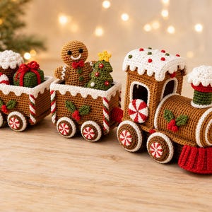 Könnte beinhalten: Ein gehäkeltes Weihnachts-Zugset bestehend aus einer braunen Lebkuchen-Lokomotive mit rotem Schienenräumer, einem Mittelwagen mit Lebkuchenmann und kleinem Tannenbaum sowie einem Endwagen mit Geschenkbox, Zuckerstange und einem Cupcake.
