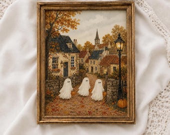 May include: A framed painting in a gold-toned frame depicting a village street scene during autumn. Three white ghost figures holding small orange pumpkins walk along a path covered in fallen leaves, surrounded by stone cottages and a street lamp.