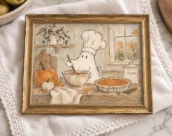 May include: A framed watercolor illustration featuring a ghost wearing a chef hat, stirring a bowl in a kitchen. The scene includes a pumpkin, a pie, a flour canister labeled FLOUR, and a window. The frame is gold with a textured finish.