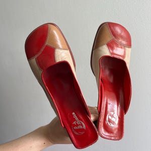 Peut inclure: Une paire de mules vintage en cuir patchwork rouge, beige et crème. Les chaussures à bout carré et à dos ouvert ont un intérieur rouge avec le logo "Bata". Les chaussures sont présentées sur un fond uni.