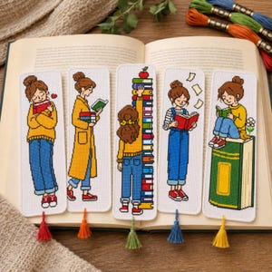 Puede incluir: Cinco marcapáginas rectangulares de tela con ilustraciones en punto de cruz de una persona de pelo castaño leyendo libros. Cada marcapáginas incluye una borla colorida en la parte inferior. Los diseños muestran varias escenas de lectura y libros.