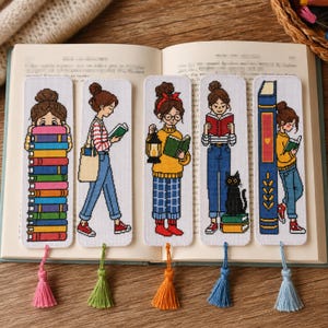May include: Five rectangular fabric bookmarks featuring cross-stitch illustrations of people reading books. Each bookmark has a unique design, including stacks of books, a black cat, and lanterns, finished with a colorful hanging tassel at the bottom.