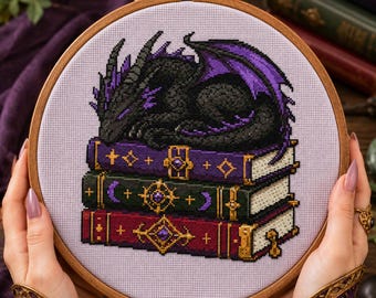 May include: A cross-stitch embroidery in a round wooden hoop featuring a black dragon with purple accents sleeping atop a stack of three books. The books are purple, dark green, and red, each decorated with gold-colored ornate metal clasps.