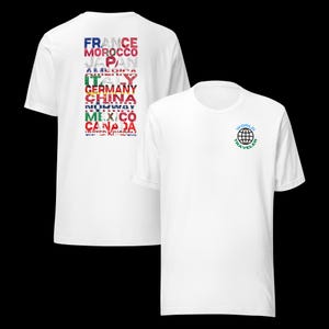 May include: A white short-sleeve t-shirt featuring a small globe graphic with the text "WORLD TRAVELER" on the front. The back displays a vertical list of country names, including France, Morocco, Japan, America, Italy, Germany, China, Norway, Mexico, Canada, and United Kingdom, each filled with its respective national flag pattern.