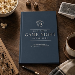 May include: A dark blue hardcover score book with gold text that reads Smith Family Game Night Score Book and Bragging Rights, Officially Documented. The cover features a small graphic of a hand of playing cards centered above the title text.