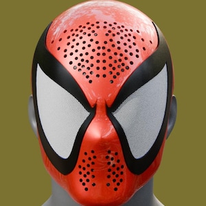 May include: A glossy red full-face mask featuring a perforated forehead and chin area for ventilation. The mask includes large, white mesh eye lenses outlined by thick black borders, creating a distinct contrast against the vibrant red surface.