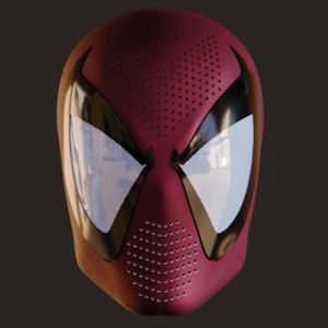 May include: A maroon full-head mask featuring large, white, mesh-covered eye lenses framed by glossy black accents. The forehead and chin areas are detailed with a pattern of small, circular ventilation holes, creating a textured appearance.