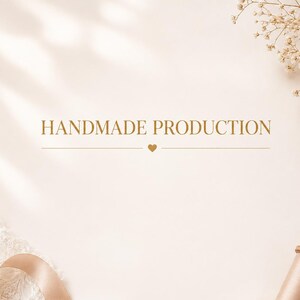 Può includere: Uno sfondo beige chiaro con il testo HANDMADE PRODUCTION in lettere maiuscole dorate e una piccola icona a forma di cuore sotto. Una bobina di nastro di raso beige chiaro e un pezzo di pizzo bianco sono posizionati negli angoli inferiori.