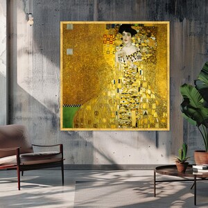 Peut inclure: Une impression d'art murale carrée représentant le Portrait d'Adele Bloch-Bauer I de Gustav Klimt. La peinture montre une femme vêtue d'une robe à motifs dorés avec des formes géométriques, sur un fond doré scintillant avec un accent vert.