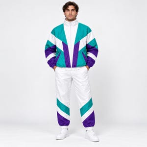 May include: A track suit featuring a jacket and pants with a color-blocked design in white, teal, and purple. The jacket has a high collar and a full-length front zipper. The pants have an elastic waistband and matching color-blocked panels.