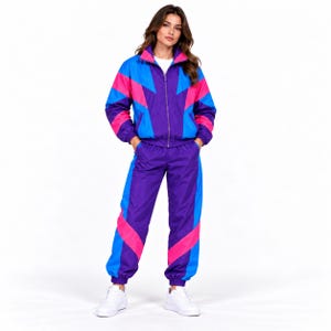 May include: A matching tracksuit set featuring a zip-up jacket and trousers in a vibrant color-blocked pattern of purple, bright blue, and hot pink. The jacket has a high collar and long sleeves, while the trousers have a relaxed fit.