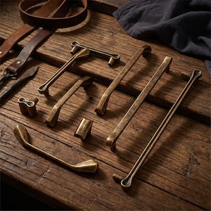 May include: A collection of antique brass cabinet hardware including various lengths of drawer pulls, handles, and knobs with a weathered finish. The set features elongated bars and small square or rounded knobs, all displaying a consistent metallic texture.