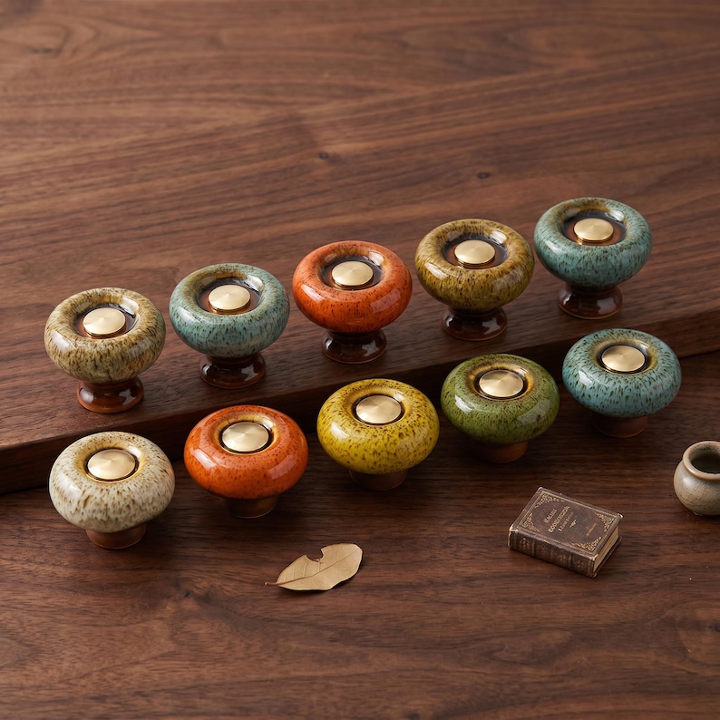 May include: A collection of ten round ceramic cabinet knobs featuring a glossy, speckled glaze in various colors including orange, yellow, green, and blue. Each knob has a smooth, circular brass-colored metal insert in the center.