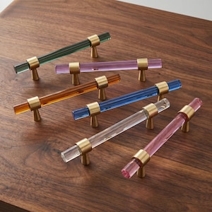 Può includere: Una collezione di sei maniglie cilindriche per armadietti con barre in acrilico traslucido nei colori verde, viola, ambra, blu, trasparente e rosa. Ogni maniglia è dotata di due supporti di montaggio in ottone spazzolato alle estremità.