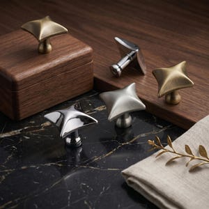 Puede incluir: Cuatro pomos para armarios en forma de estrella con varios acabados, incluyendo latón cepillado, cromo pulido y níquel cepillado. Cada pomo presenta un diseño cuadrado de cuatro puntas con un vástago central en tonos metálicos.