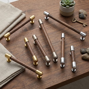May include: A collection of cabinet pulls featuring cylindrical dark wood handles with metallic end caps in brushed gold, polished silver, and matte nickel finishes. The hardware set includes various lengths, showcasing a mix of warm wood tones and polished metal accents for furniture or cabinetry applications.