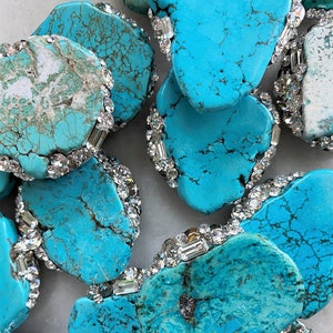 May include: Turquoise stones with a unique, marbled pattern are surrounded by a border of clear rhinestones. The stones are various shapes and sizes.