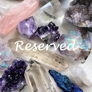 May include: A collection of crystals and gemstones, including amethyst, rose quartz, clear quartz, and iridescent agate. The crystals are arranged on a white surface and the word "Reserved" is written in white text across the image.