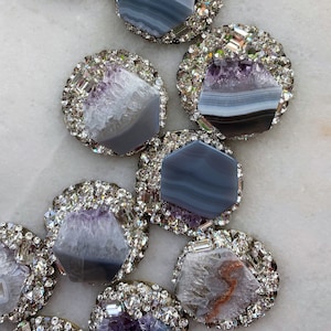 May include: A collection of hexagonal agate slices, each with a unique pattern of gray and purple, surrounded by a border of sparkling rhinestones.
