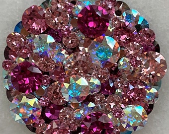May include: A circular, jeweled brooch with a cluster of pink and purple crystals. The crystals vary in size and reflect light, creating a sparkling effect. The text "Style 1." is in the upper left corner.
