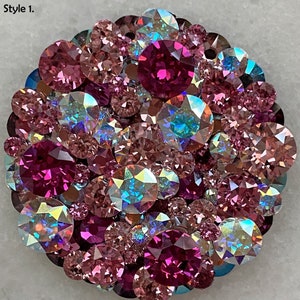 May include: A circular brooch adorned with a collection of pink and purple crystals. The crystals, of varying sizes, reflect light, producing a sparkling effect. The text "Style 1." is visible in the upper left corner.