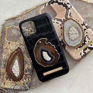 May include: Three different phone cases with a gold agate design. The cases are black, brown, and beige with a snakeskin pattern. The text "DEAL OF SWEDEN" is on the bottom of the brown case.