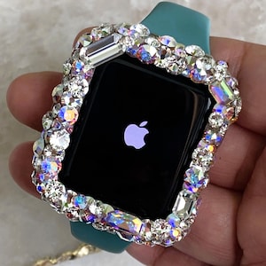 Könnte beinhalten: Eine Apple Watch mit einem türkisfarbenen Armband und einer funkelnden, irisierenden, mit Kristallen besetzten Lünette. Das Zifferblatt der Uhr ist schwarz mit dem weißen Apple-Logo. Die Kristalle sind in verschiedenen Formen und Größen.