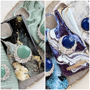 May include: Three different phone cases with marble patterns and jeweled rings. The cases are black, green, and blue with gold accents. The rings are adorned with green, blue, and clear stones.