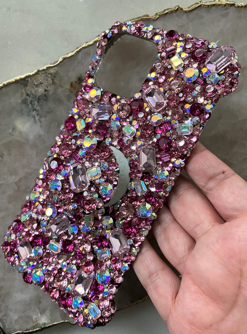 May include: A pink and iridescent rhinestone phone case with a ring holder.