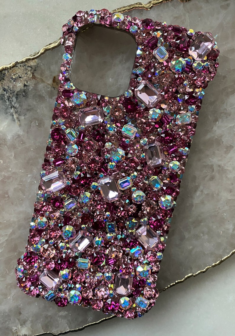 May include: A pink and purple jeweled phone case with a variety of rhinestones and crystals.