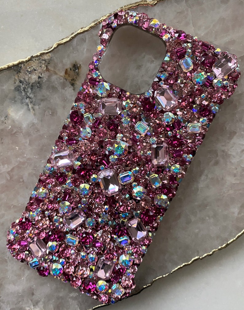 May include: A pink and purple rhinestone phone case with a variety of crystal shapes and sizes.