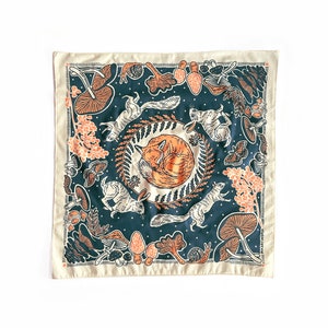 May include: Square bandana with a forest-themed design. The center features a sleeping fox surrounded by a wreath. Squirrels, rabbits, mushrooms, and butterflies are scattered around the fox on a dark blue background, with a cream-colored border.
