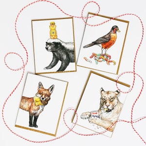 May include: Four illustrated greeting cards featuring animals. The first card shows a honey badger wearing a honey bear hat. The second card shows a robin with a worm in its beak. The third card shows a fox wearing a yellow scarf. The fourth card shows a cougar eating a candy bar.