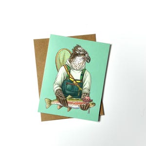 May include: A greeting card featuring a cartoon illustration of an osprey wearing overalls and holding a trout. The osprey is wearing a fishing net on its back and has a fishing lure in its beak. The card has a light green background.