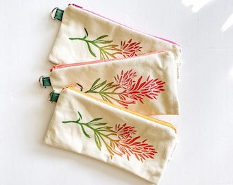 May include: Three canvas pencil cases with floral designs. Each case has a different colored zipper: pink, orange, and yellow. The floral design is a gradient of green, orange, and red. Each case has a green loop.