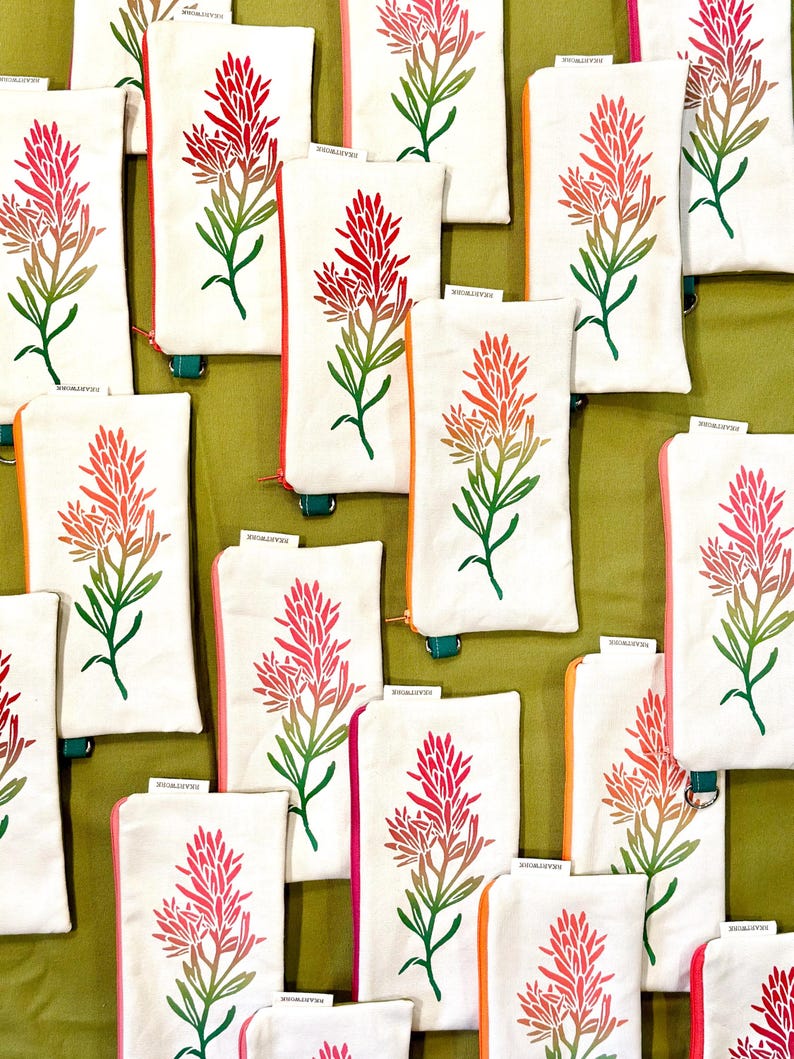 Op de afbeelding: Witte canvas pouches met een kleurrijk bloemmotief. De pouches hebben een rode, roze en oranje bloem met groene bladeren en stelen. De ritsen en randen zijn in verschillende kleuren, waaronder roze, oranje en groen.