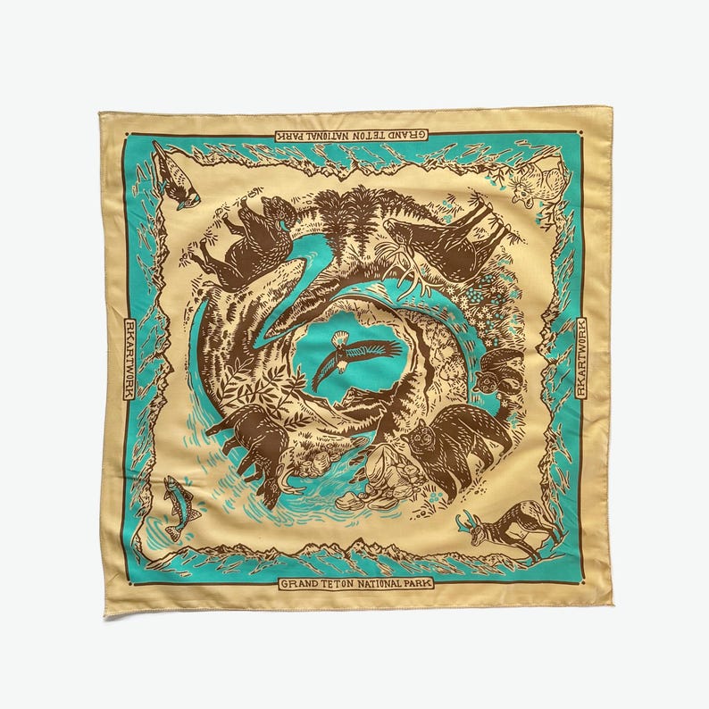 Peut inclure: Un bandana jaune avec une bordure turquoise repr&eacute;sentant un motif circulaire d'animaux et de plantes. Le texte "Grand Teton National Park" est imprim&eacute; en bas du bandana.