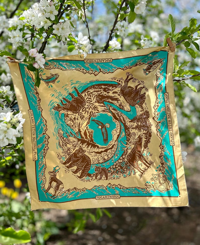Peut inclure: Un bandana jaune avec une bordure turquoise repr&eacute;sentant un motif d'animaux et de plantes du parc national de Grand Teton. Le bandana porte l'inscription "RKARTWORK" et "GRAND TETON NATIONAL PARK".