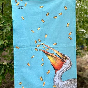 May include: A blue tea towel with a white pelican with an open beak catching goldfish. The text "Remarkable by Roberts" is printed in the top left corner.