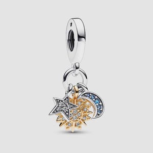 May include: A silver-toned charm featuring a central gold-toned sun with clear stones, a silver star with clear stones, and a silver crescent moon with blue stones. The charm hangs from a silver bail, creating a layered celestial design.