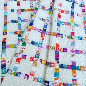 Pu&ograve; includere: Una trapunta patchwork caratterizzata da una griglia di quadrati di tessuto colorati e fantasia, separati da strisce di tessuto color crema. Il tessuto color crema &egrave; decorato con un motivo ripetuto di piccoli cuori bianchi e cuciture trapuntate.