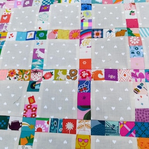 Pu&ograve; includere: Una trapunta patchwork con blocchi alternati di tessuto grigio chiaro con un motivo a cuori bianchi e strisce di quadrati di tessuto colorati. I quadrati colorati mostrano varie illustrazioni, tra cui fragole, fiori, animali e forme geometriche.