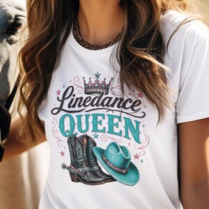 Könnte beinhalten: Ein weißes T-Shirt mit einem Grafikdruck, der den Text Linedance QUEEN, eine Krone, ein Paar schwarze Cowboystiefel mit Sporen und einen türkisfarbenen Cowboyhut zeigt. Das Design enthält dekorative rosa Sterne und Schnörkel um den Text.